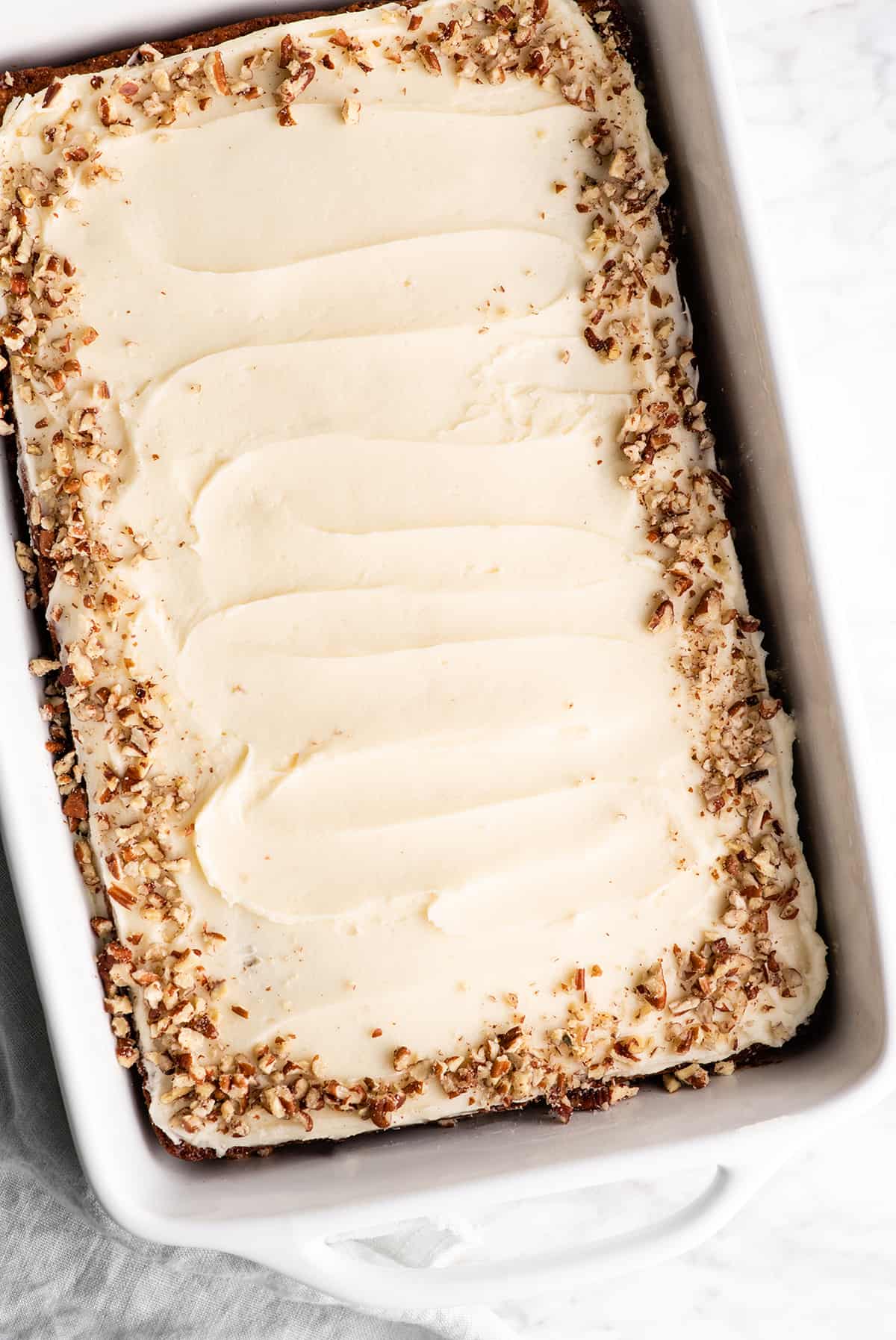 overhead view of a frosted banana cake in a pan with nuts around the edge