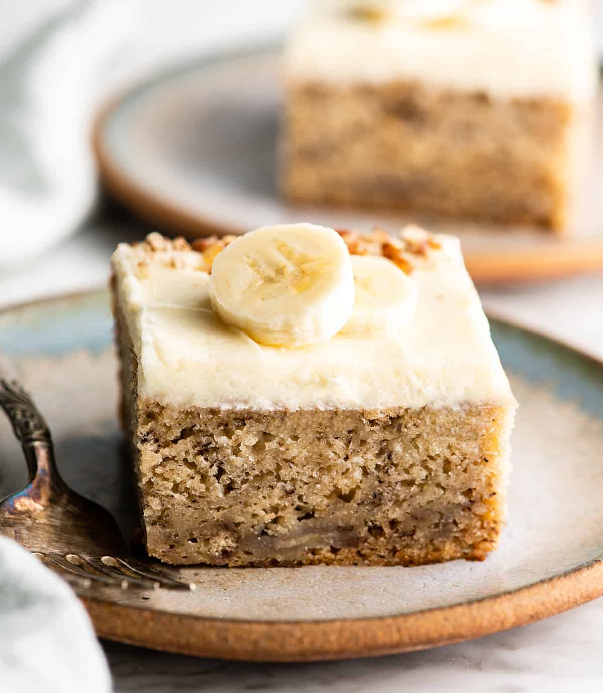 front view of a piece of banana cake with cream cheese frosting on a plate
