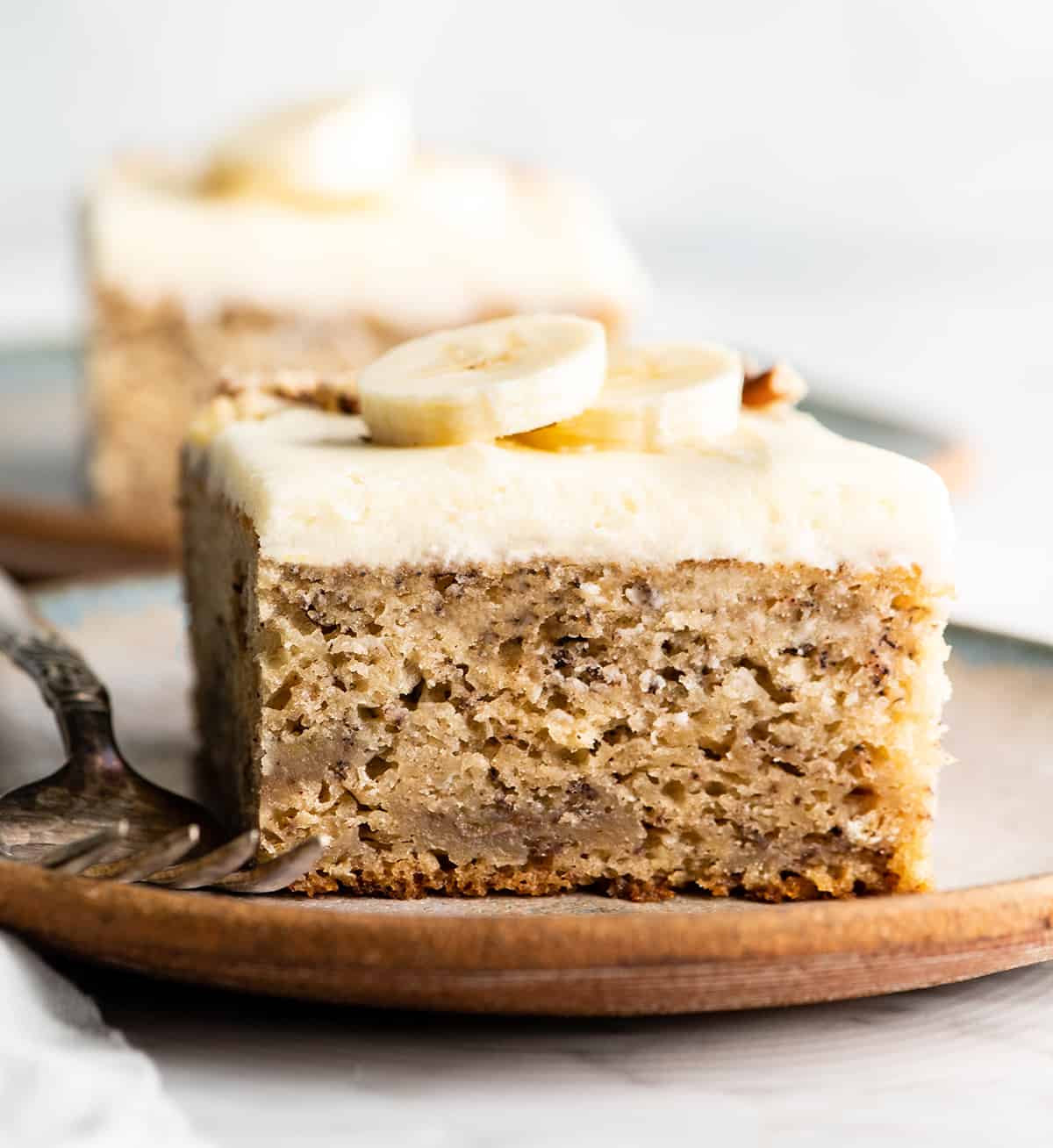 This is the best banana cake recipe ever! It's easy to make (no mixer required), moist, loaded with bananas and topped with a delicious cream cheese frosting. front view of a slice of banana cake with cream cheese frosting