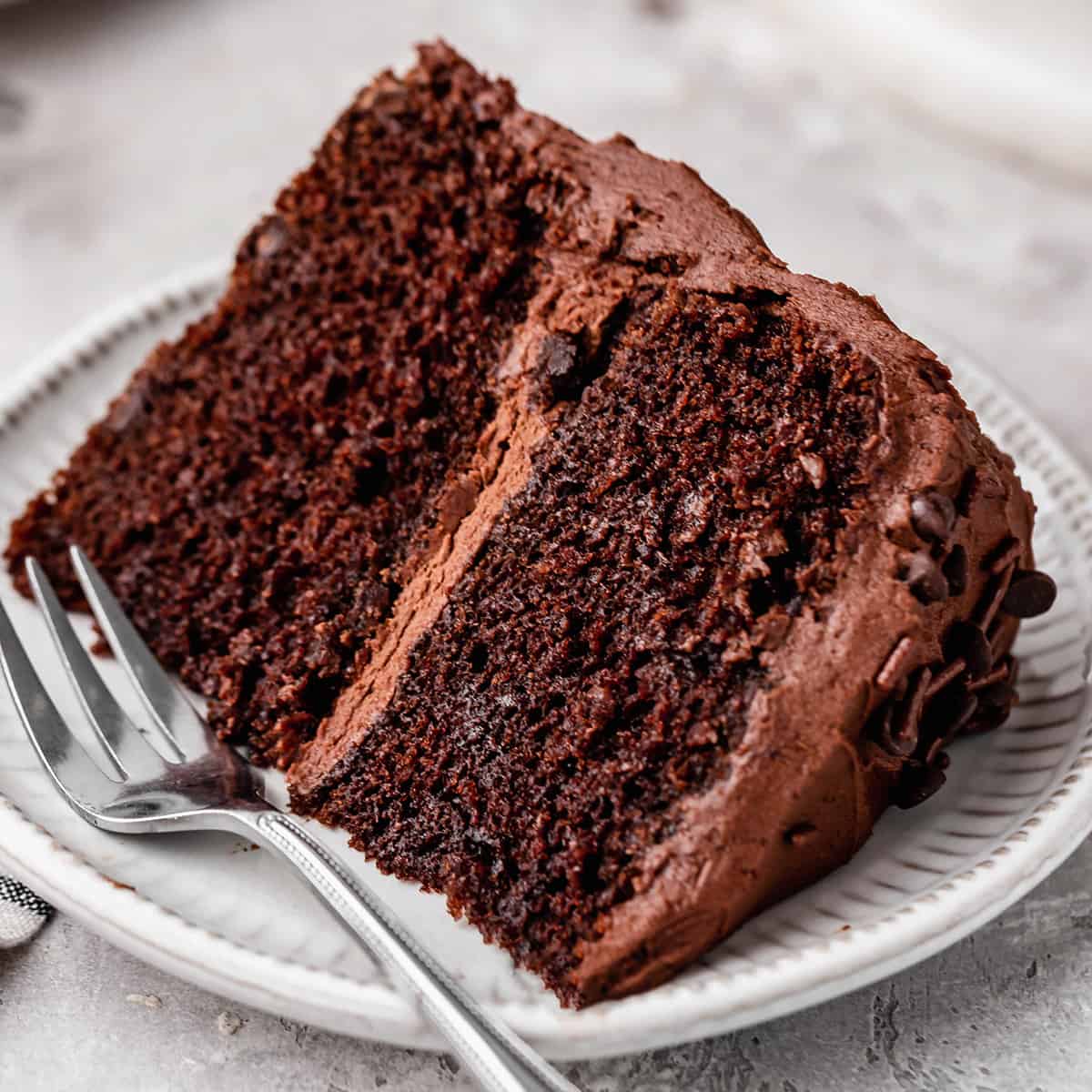 This is the best chocolate cake recipe for serious chocolate lovers. It's dense and moist with a perfect crumb! Topped with chocolate buttercream frosting it's the ultimate chocolate birthday cake. Check out the step-by-step photos and watch the video to learn how to make this easy chocolate cake recipe and ditch boxed cake mixes once and for all! a slice of chocolate cake on a plate with a fork