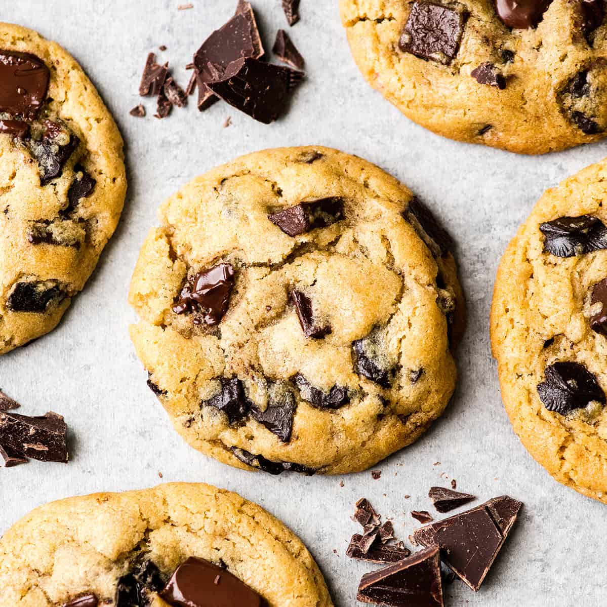 This is the best chocolate chip cookie recipe ever. No funny ingredients, no chilling time, etc. Just a simple, straightforward, amazingly delicious, doughy yet still fully cooked, chocolate chip cookie that turns out perfectly every single time! #cookies #chocolatechipcookies #baking #recipe #chocolate Overhead view of one chocolate chip cookie surrounded by four other chocolate chip cookies and chopped chocolate