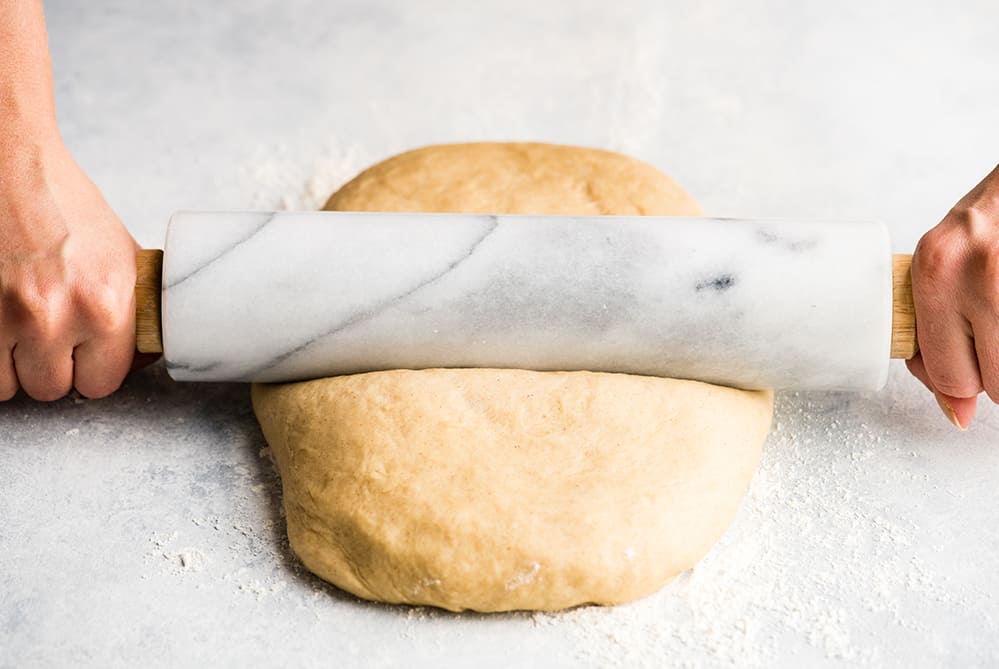 front photo of hands rolling cinnamon roll dough 