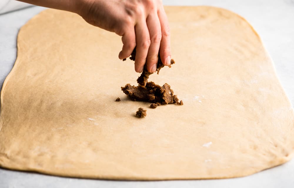 cinnamon sugar filling being sprinkled onto cinnamon roll dough