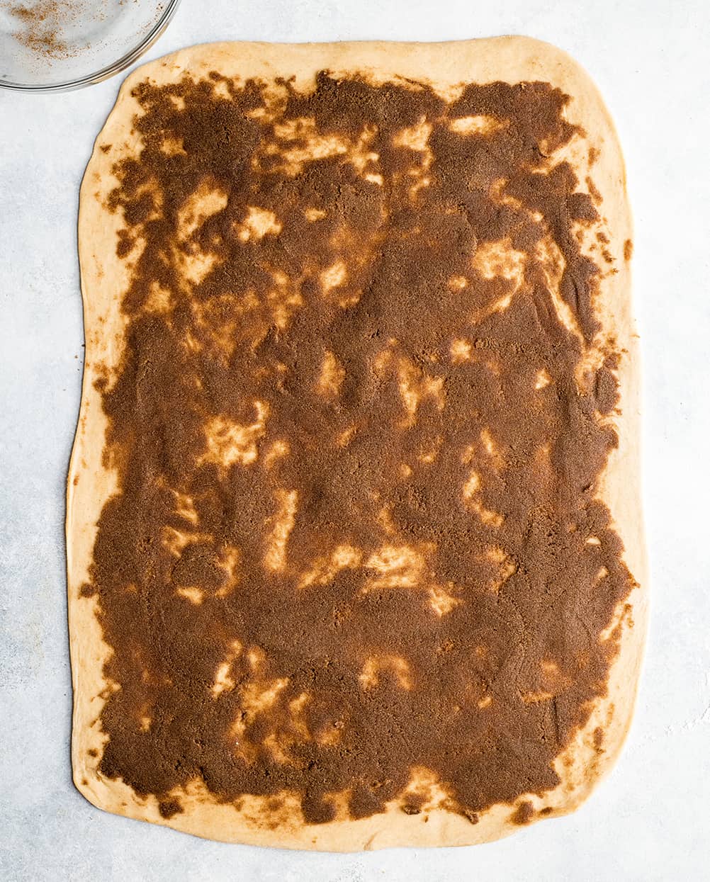 overhead photo showing how to make cinnamon rolls - cinnamon sugar filling spread evenly over dough