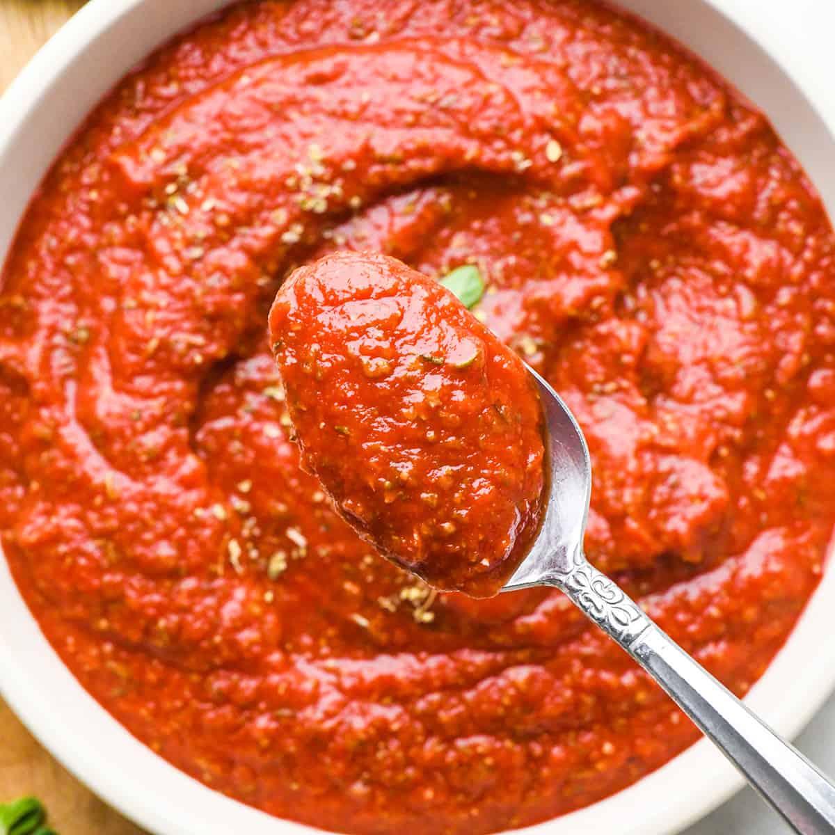 a spoon holding a scoop of pizza sauce over a bowl of pizza sauce