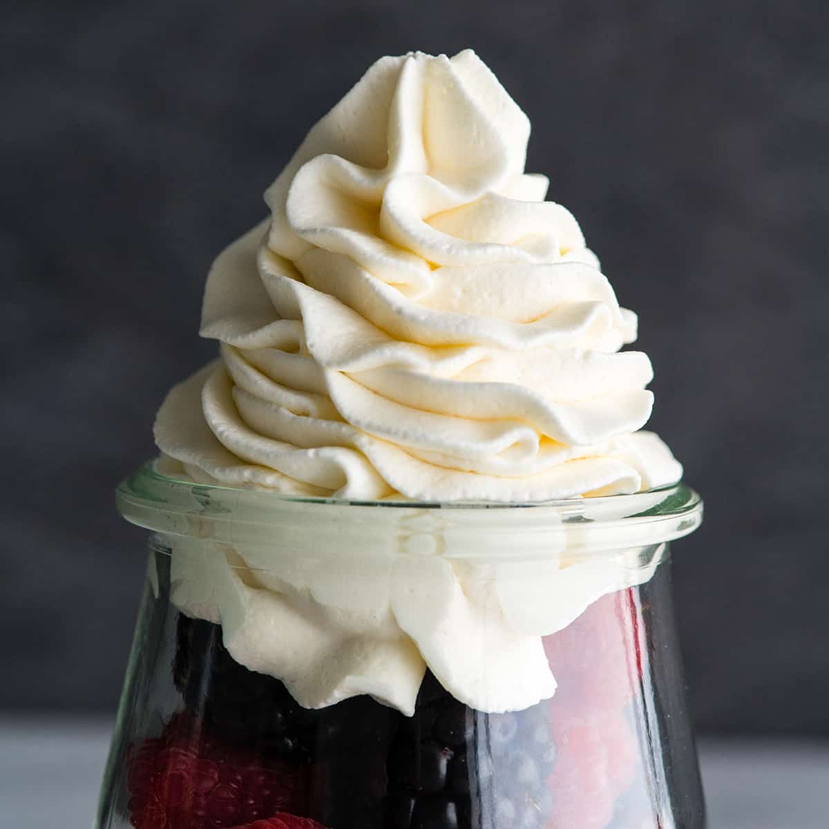 Homemade whipped cream is easy to make with only 3 ingredients in 5 minutes and it's so delicious you'll ditch the store-bought stuff for good once you try it! Watch the video and follow our step-by-step photos to learn how to make the best homemade whipped cream recipe! #whippedcream #heavycream #homeamdewhippedcream #joyfoodsunshine #whippedcreamrecipe Font view of homemade whipped cream piped on top of fresh berries