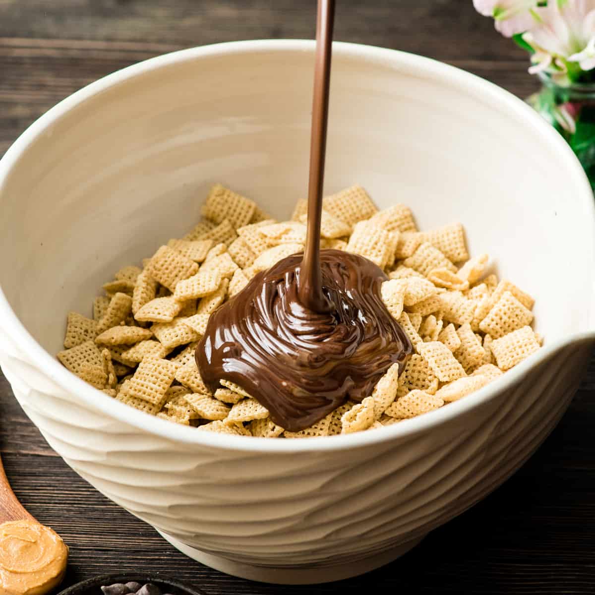 front view showing how to make puppy chow - pouring melted chocolate mixture onto cereal in a bowl