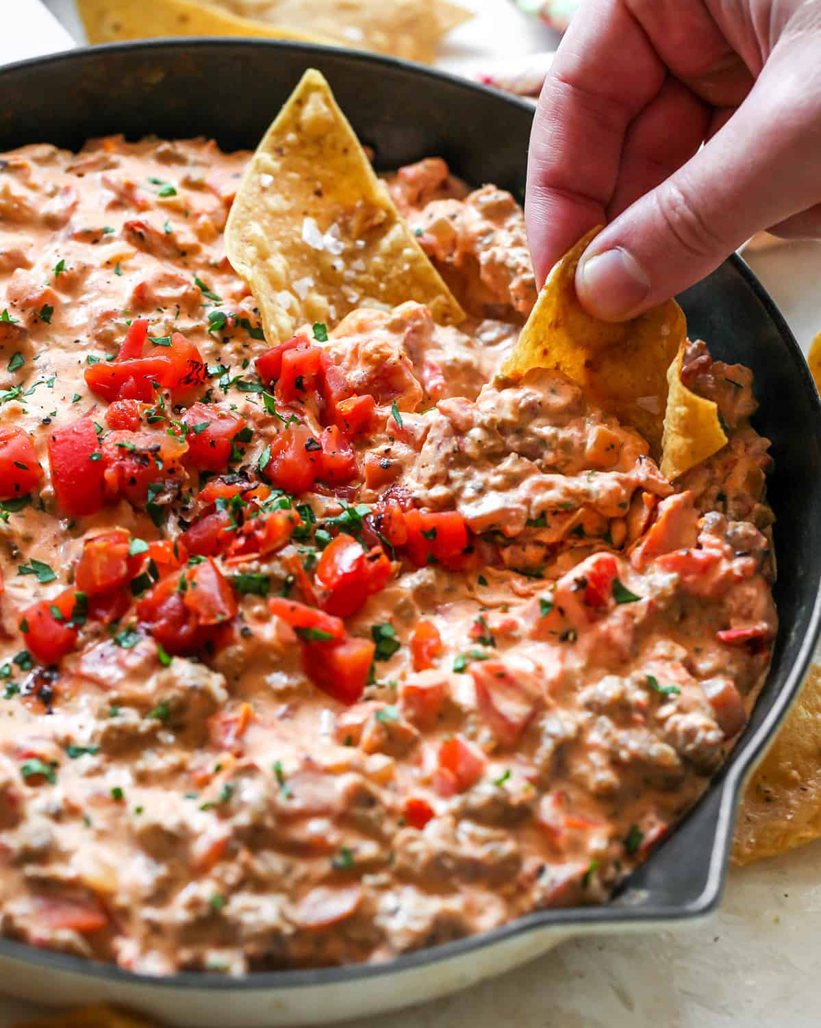 front view of a chip being dipped into a skillet of Cream Cheese Sausage Dip