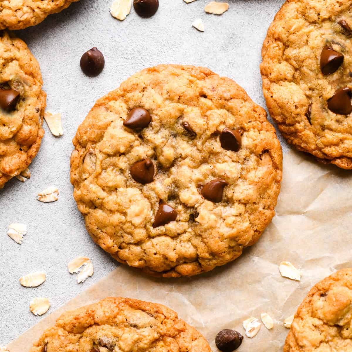 6 Chocolate Chip Oatmeal Cookies on parchment paper with raw oats and chocolate chips around them
