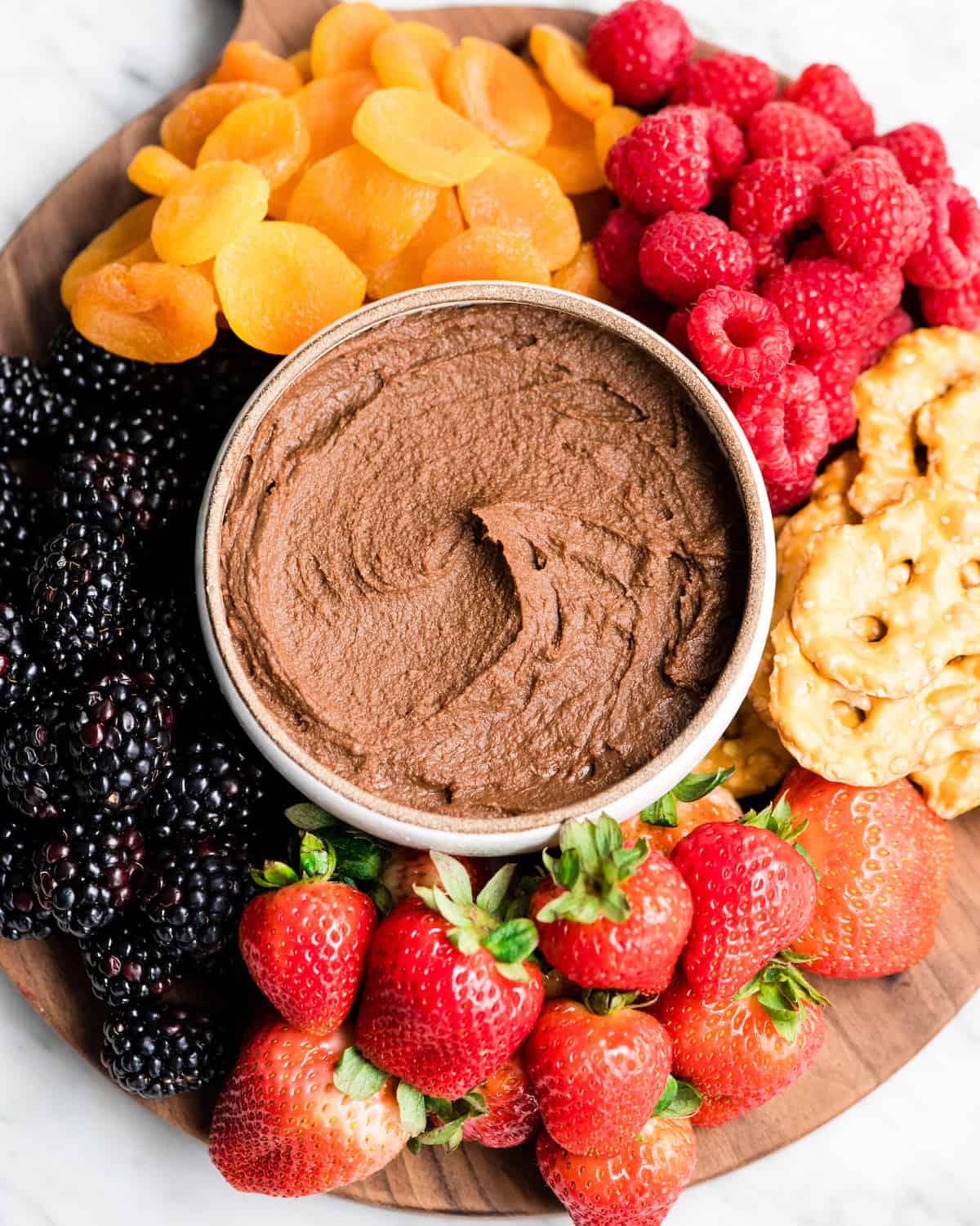 Overhead view of a cheese board loaded with fruit, pretzels, etc. with a bowl of Chocolate Hummus in the middle
