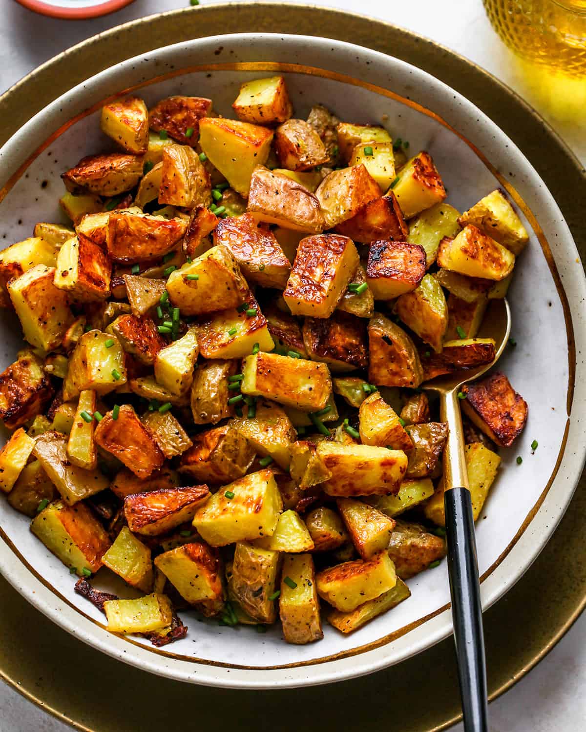 crispy Oven Roasted Potatoes in a serving bowl with a spoon garnished with chives