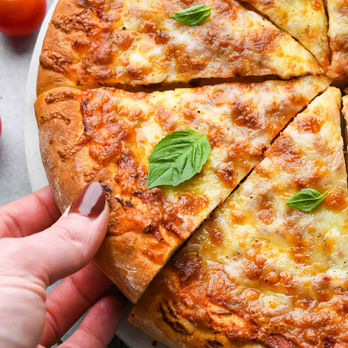 a hand taking a triangular slice of pizza made with this Pizza Dough Recipe garnished with basil 