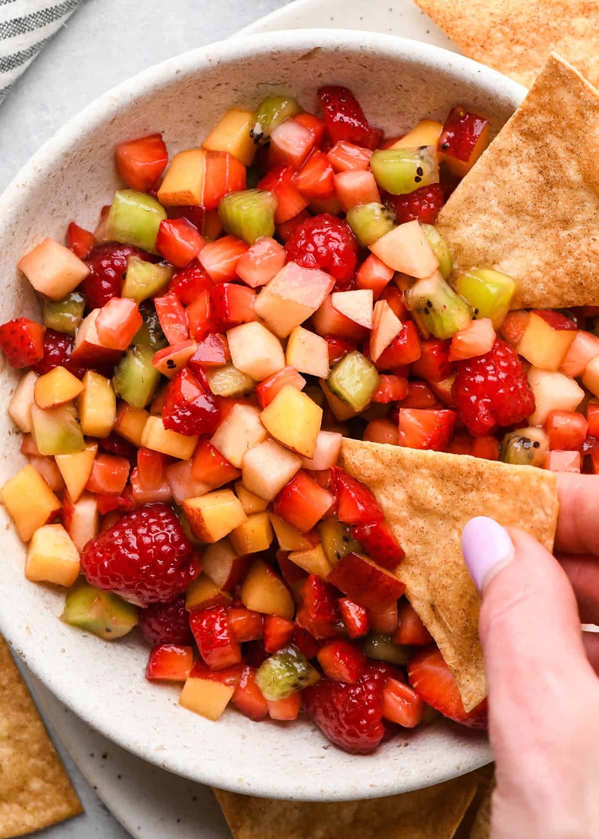 a cinnamon chip being dipped into fruit salsa 