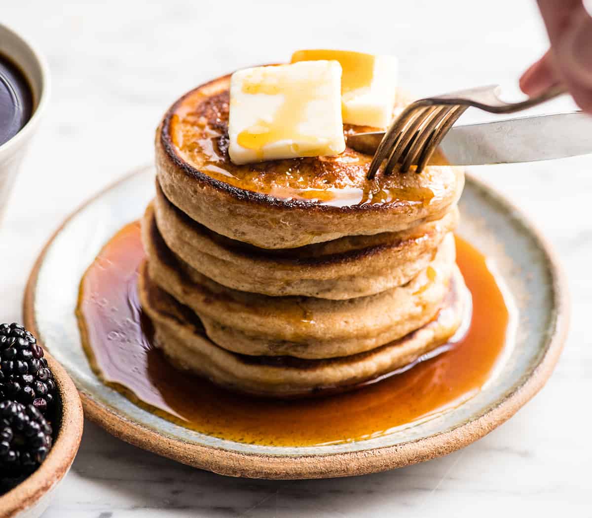 front view of a stack of four greek yogurt pancakes on a plate being cut into with a knife and fork