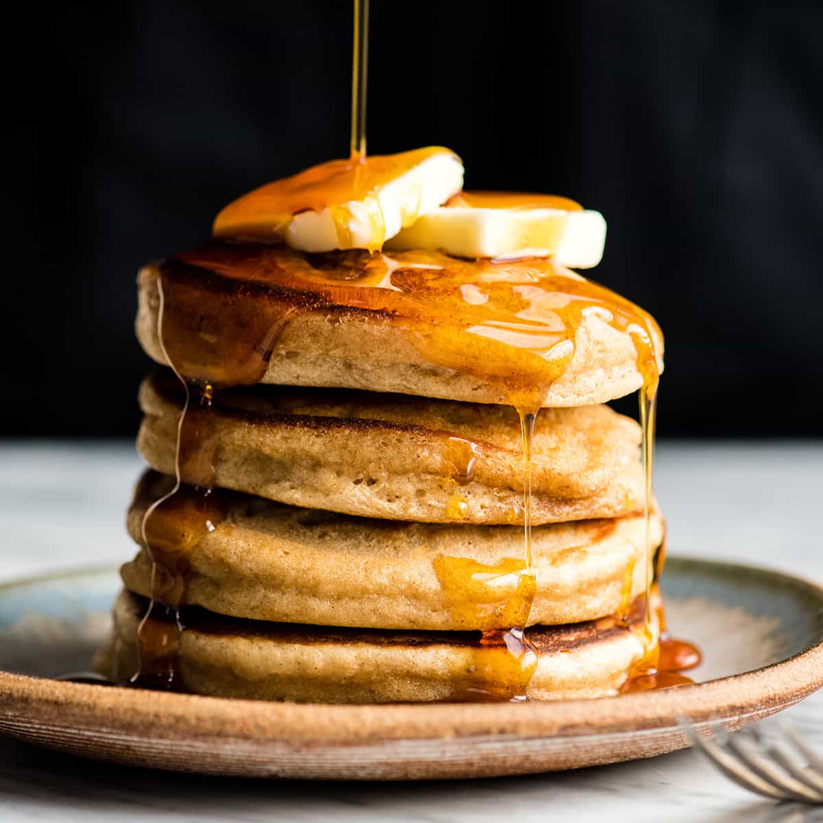 Healthy Greek Yogurt Pancakes Recipe! An easy, one-bowl, delicious and nutritious breakfast recipe that your whole family will love! Freezer-friendly with gluten-free and refined sugar free options!! #easybreakfast #pancakes #recipe #greekyogurt #breakfast #vitamix #healthy Front view of syrup being poured on a stack of four Greek Yogurt Pancakes with butter on top.