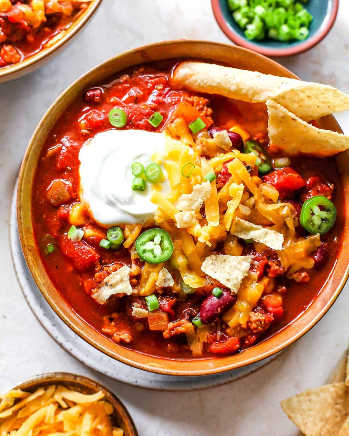 overhead view of a bowl of turkey chili with sour cream, cheese, chips and green onions