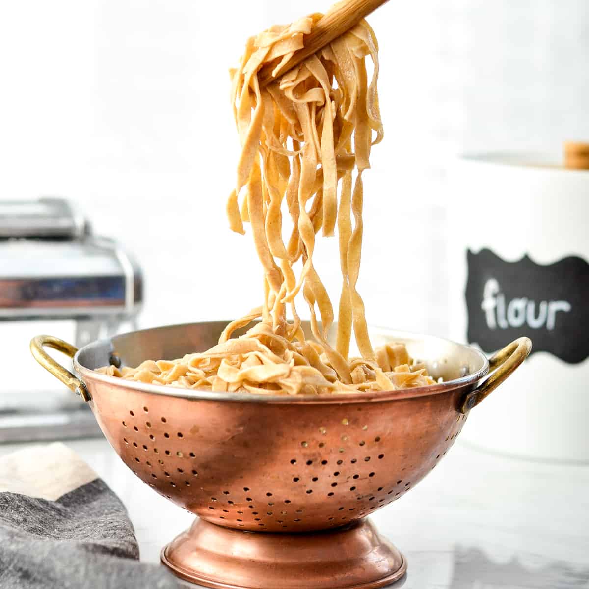 This Homemade Whole Wheat Pasta is the best homemade pasta recipe that taste's worlds better better than boxed varieties! Use it in a delicious main dish or serve it as a yummy side! #homemade #pasta #wholewheat #homemadenoodles #pastamaker Front view of cooked Homemade Whole Wheat Pasta being pulled out of a colander with wooden tongs