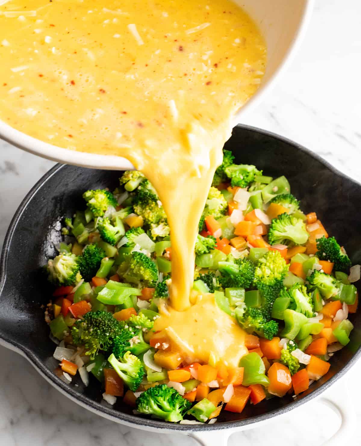 photo showing how to make a frittata recipe pouring egg mixture into cooked vegetables