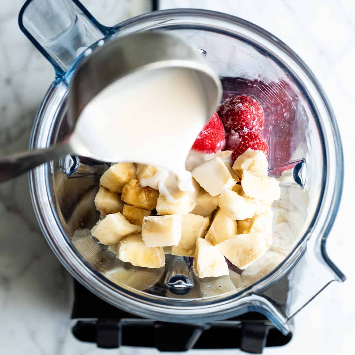 overhead photo showing how to make a smoothie bowl - adding almond milk before blending