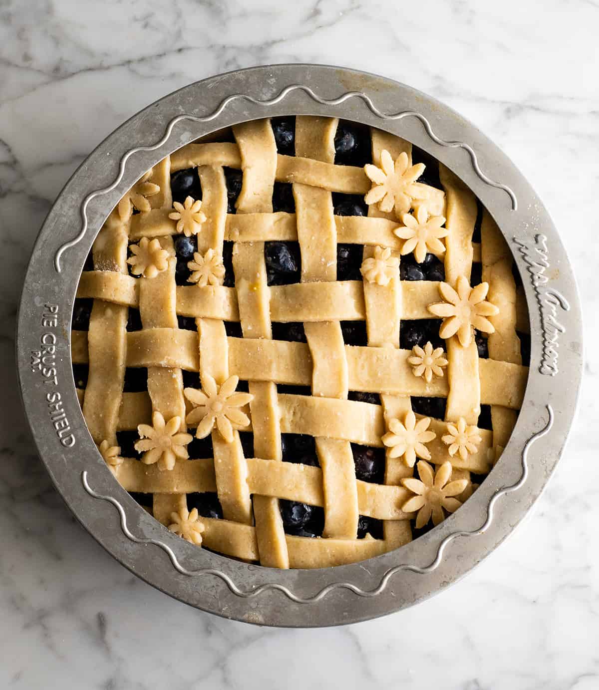 overhead view of a blueberry pie before baking with a pie crust shield around the edge