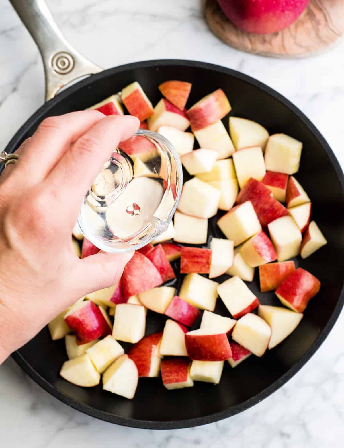 overhead view of a hand pouring water into diced apples in a nonstick fry pan showing how to make cinnamon apples