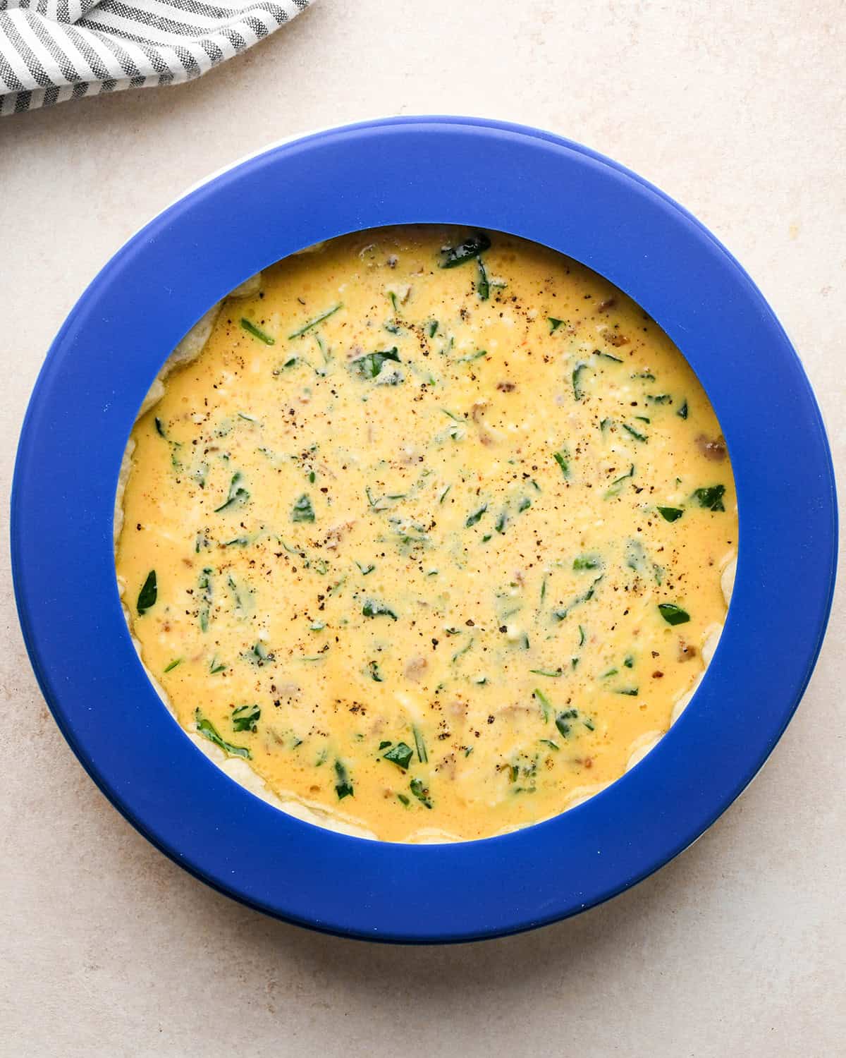 bacon spinach quiche in a pie dish before baking with a pie crust shield
