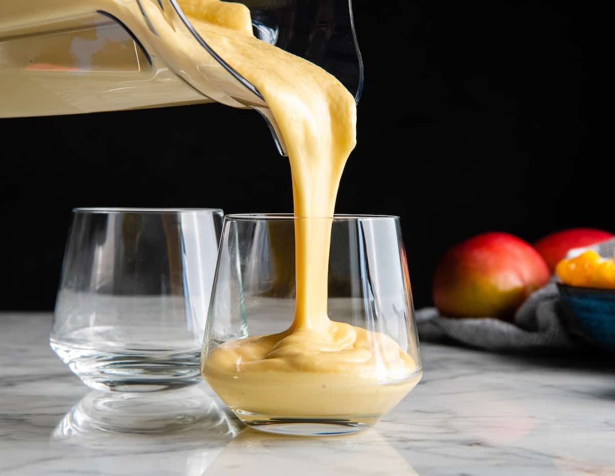front view of mango smoothie being poured into a glass from the blending container