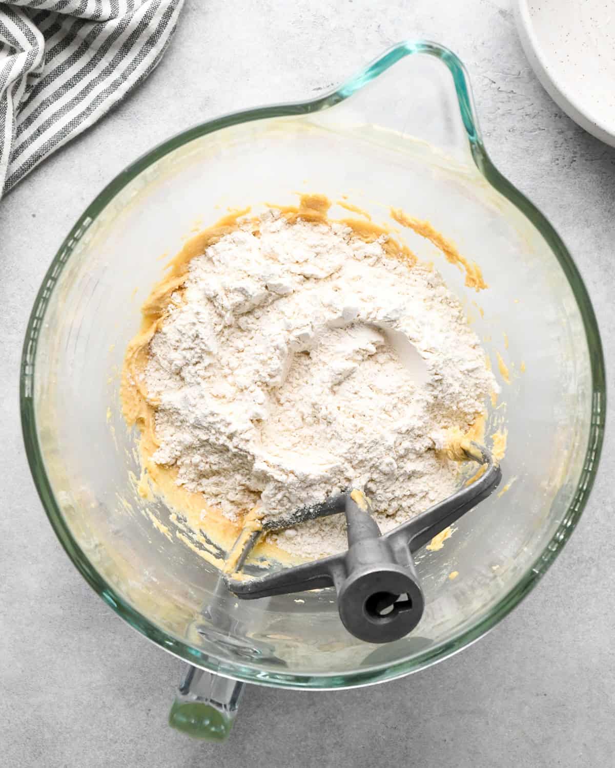 making chocolate chip oatmeal cookies - flour mixture added to the wet ingredients before beating in a glass mixing bowl with a paddle attachement and striped towel in the top left corner 