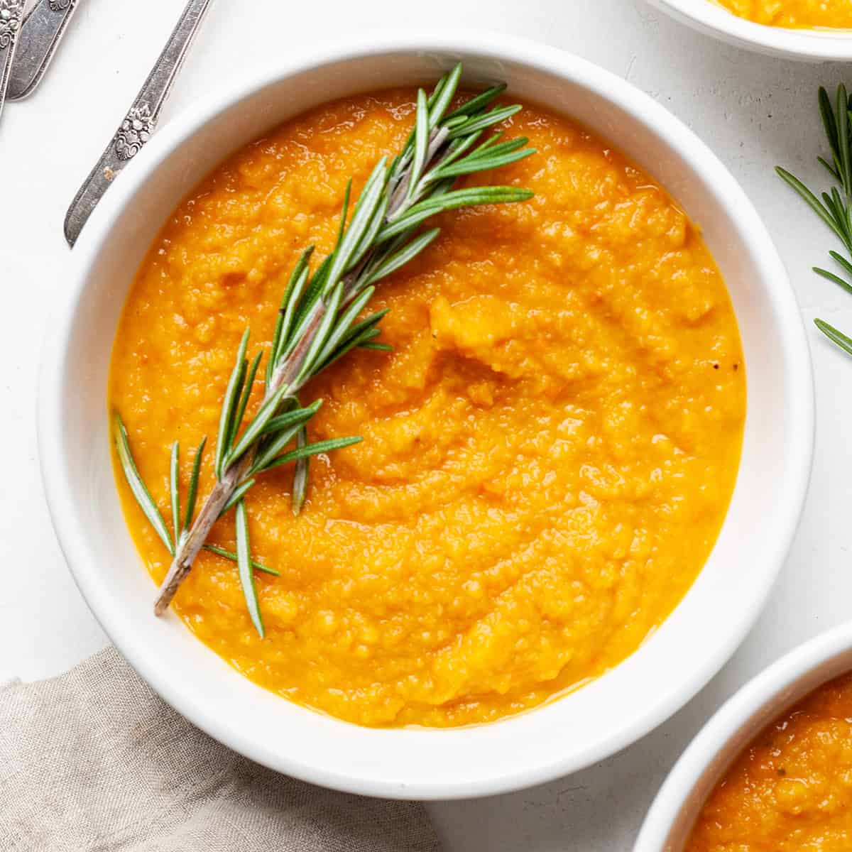 Roasted Root Vegetable Soup with butternut squash, sweet potatoes, parsnips & carrots! The perfect healthy fall soup recipe! Gluten-Free, dairy-free, vegan, & paleo! #vegetablesoup #soup #vitamix #roastedvegetables #sweetpotato #butternutsquash #vegan #paleo #whole30 #glutenfree #dairyfree #sugarfree a bowl of roasted vegetable soup garnished with fresh rosemary