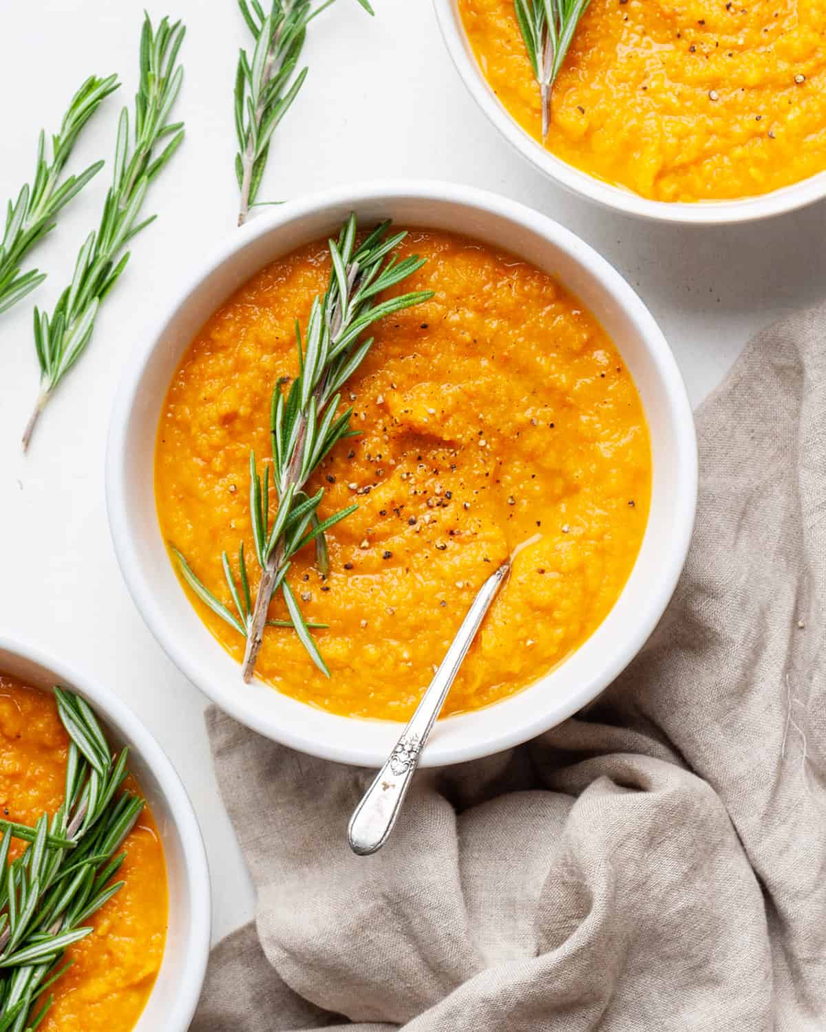 a bowl of roasted vegetable soup garnished with fresh rosemary