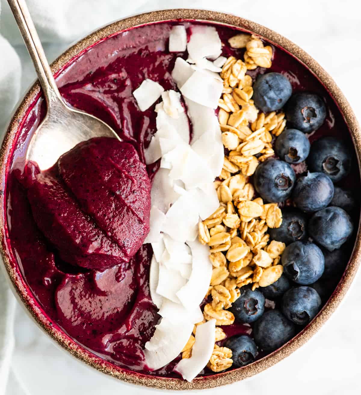 Overhead view of an acai smoothie bowl with toppings and a spoon taking a bite out of it