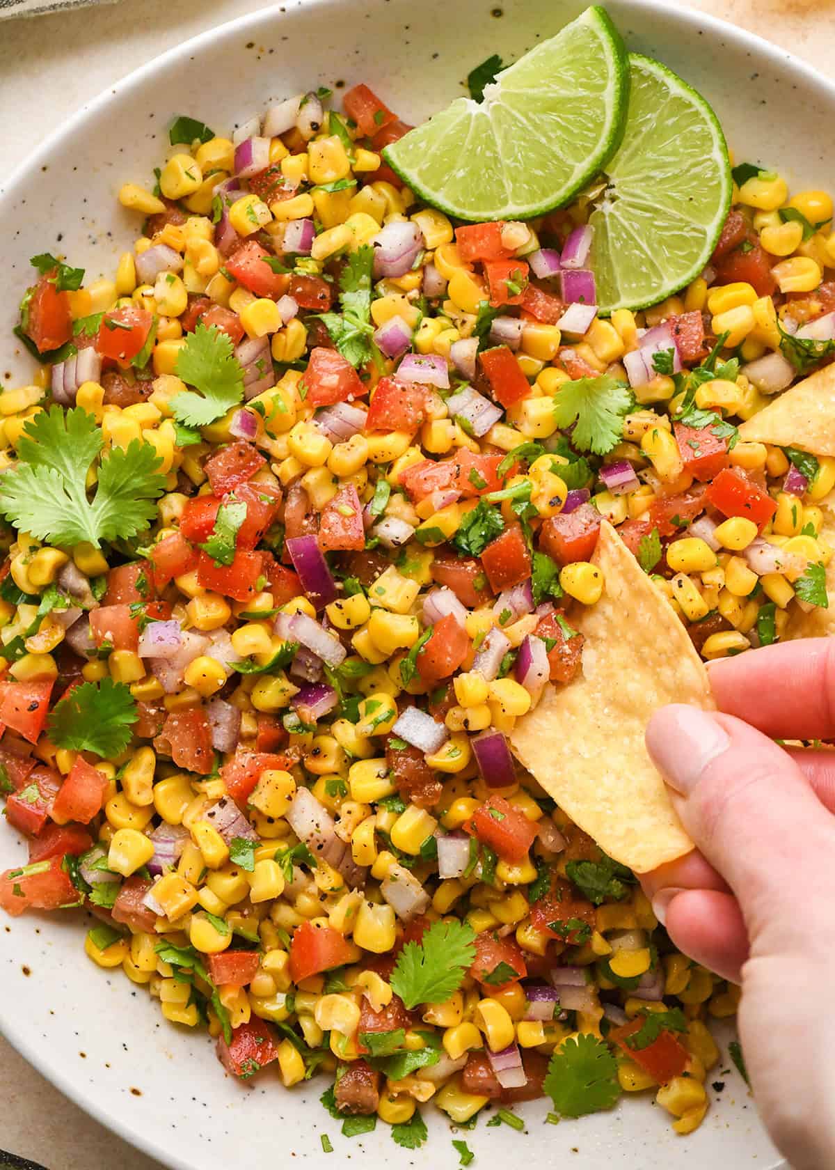 a chip taking a dip of Corn Salsa in a bowl