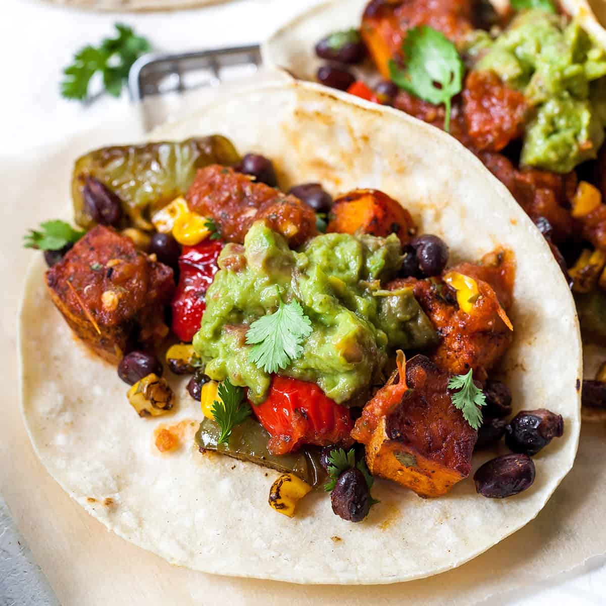 These healthy black bean sweet potato tacos are the best vegetarian tacos ever. Sweet potatoes and vegetables are perfectly spiced and roasted, then tossed with a honey, lime cilantro mixture for the most flavorful and delicious tacos. Taco night isn't complete without this sweet potato taco recipe! overhead view of black bean sweet potato tacos
