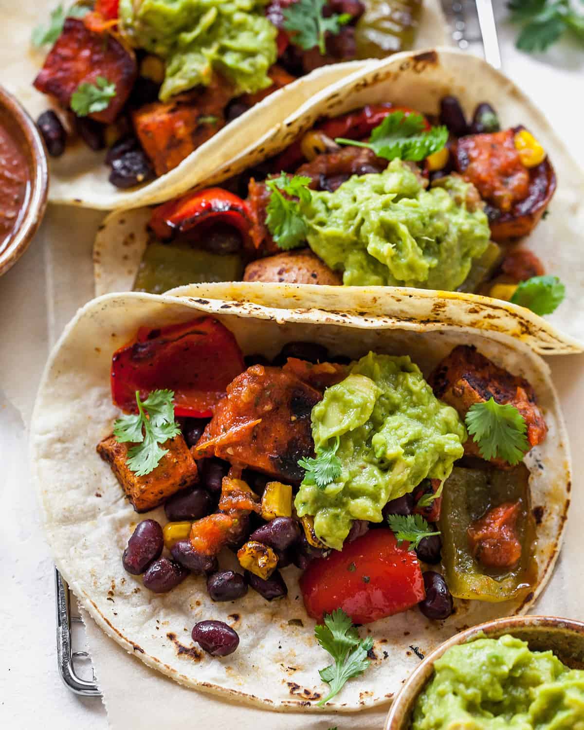 These healthy black bean sweet potato tacos are the best vegetarian tacos ever. Sweet potatoes and vegetables are perfectly spiced and roasted, then tossed with a honey, lime cilantro mixture for the most flavorful and delicious tacos. Taco night isn't complete without this sweet potato taco recipe! overhead view of three black bean sweet potato tacos with guacamole