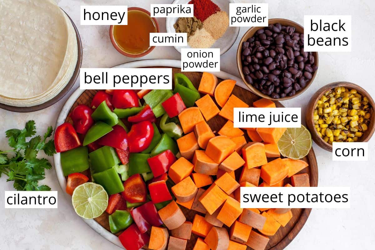 These healthy black bean sweet potato tacos are the best vegetarian tacos ever. Sweet potatoes and vegetables are perfectly spiced and roasted, then tossed with a honey, lime cilantro mixture for the most flavorful and delicious tacos. Taco night isn't complete without this sweet potato taco recipe! overhead view of the labeled ingredients in this sweet potato tacos recipe