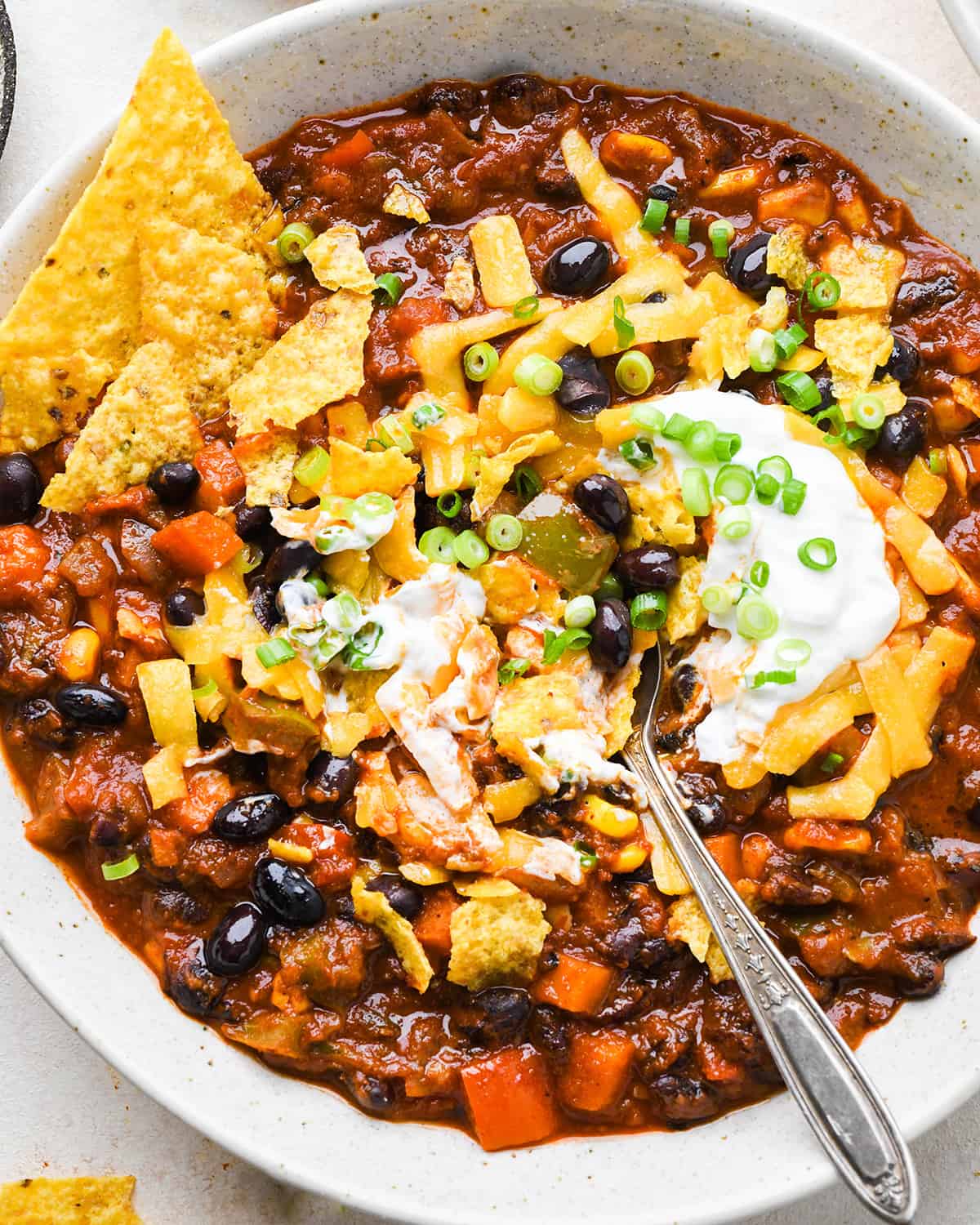 a bowl of Vegetarian Chili with sour cream, cheese, chips and chives. 